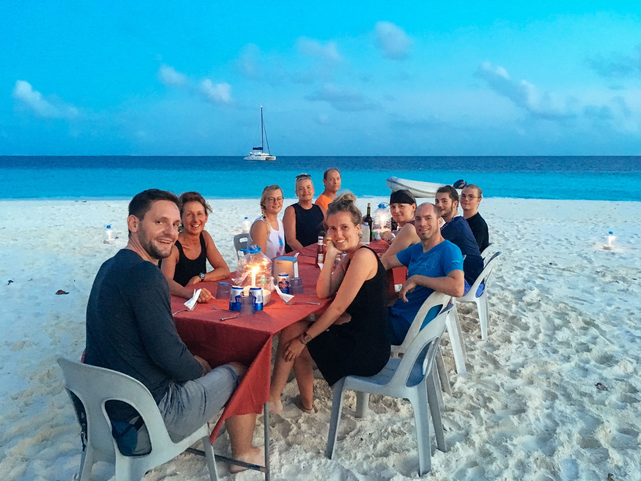 Cena sulla spiaggia al tramonto su un atollo delle Maldive, con tavolo apparecchiato sulla sabbia.